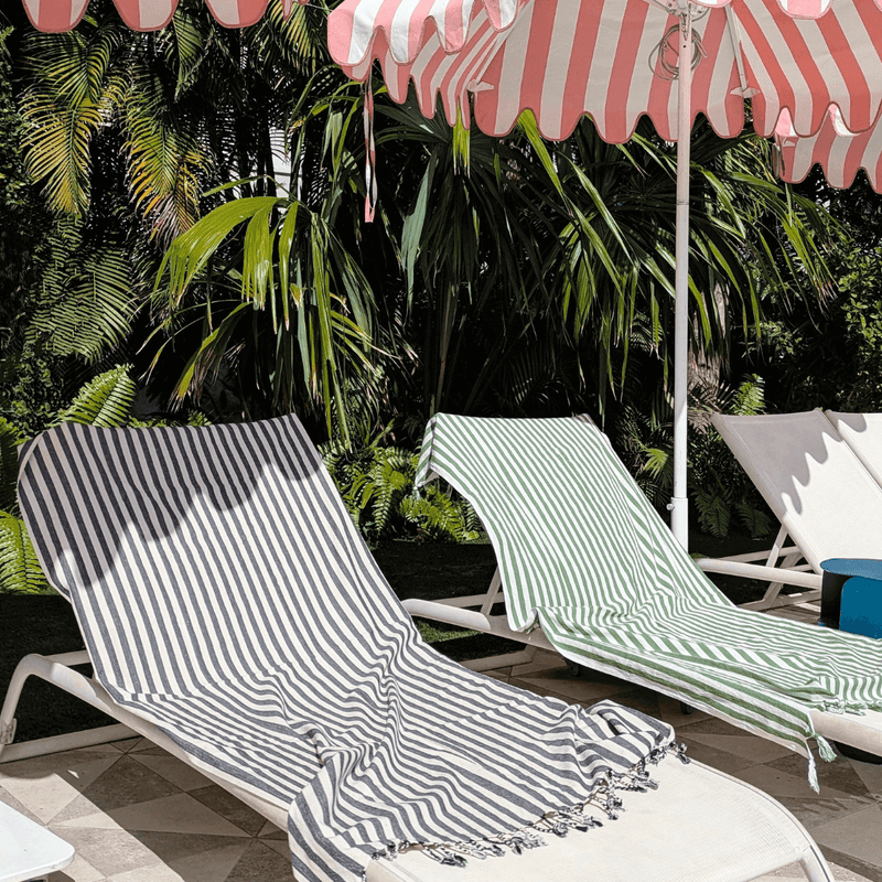one black and one green striped turkish towel pestemal on lounge chairs by the pool with sun umbrellas   