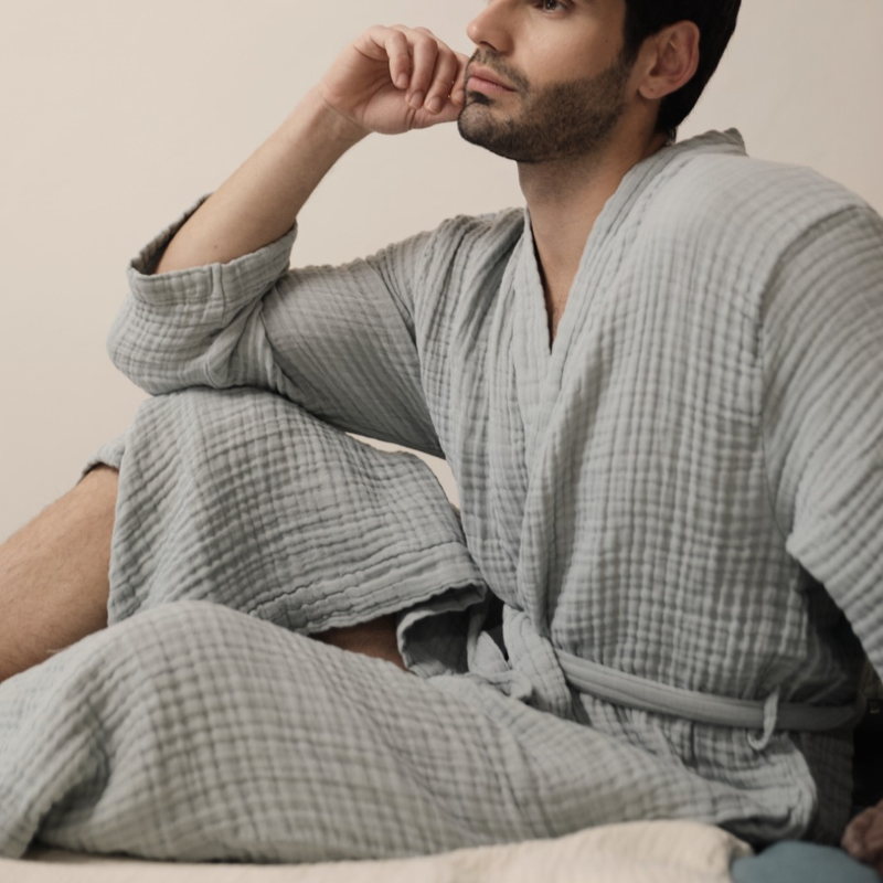 A man relaxing in a Crinkle Gauze Bathrobe Jasper, showcasing the soft and breathable fabric.