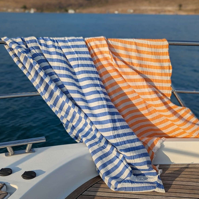 orange and blue colour muslin turkish towels hanging on the deck of the boat moving with the wind 
