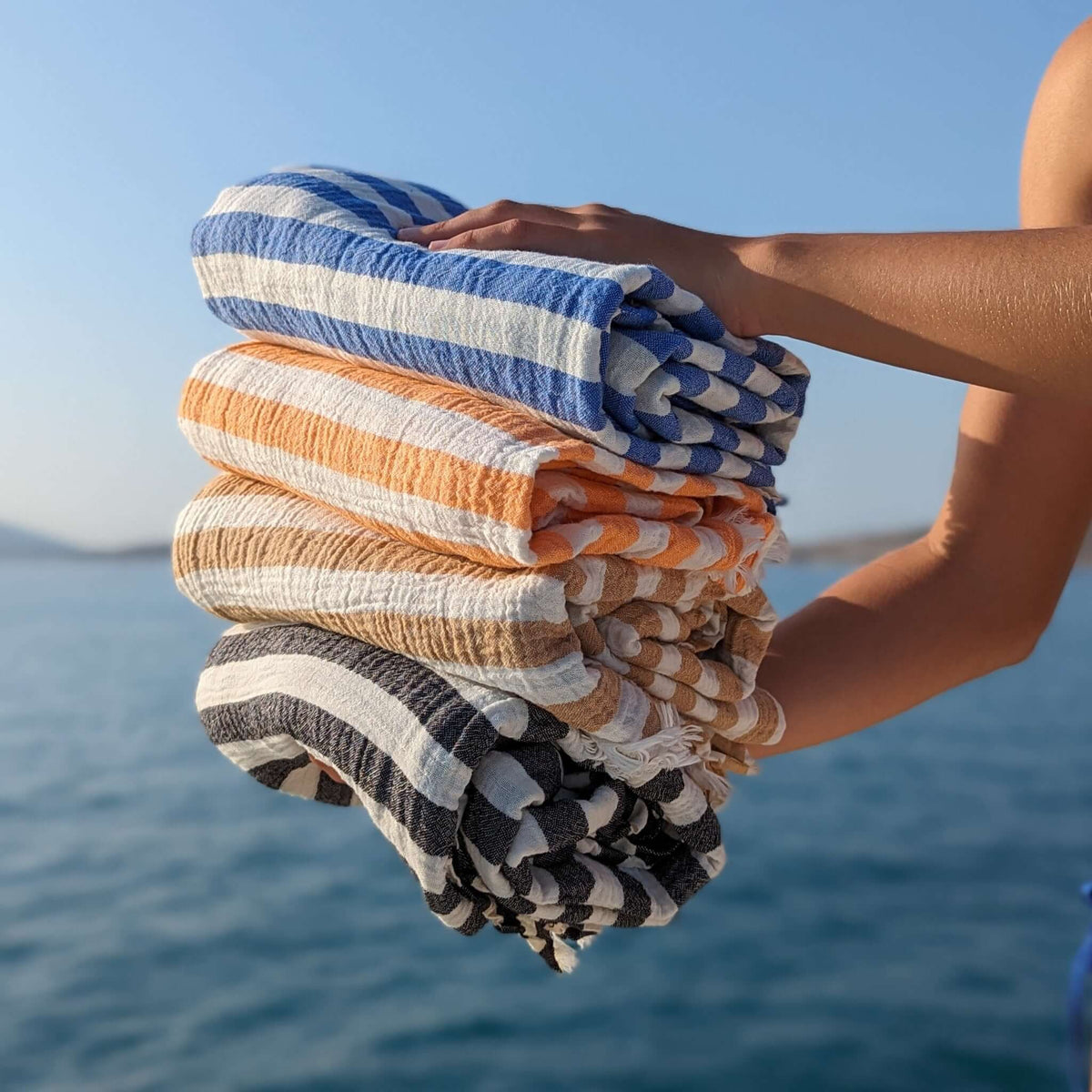 set of 4 muslin turkish beach towels blue orange brown black stripes on white on the boat with the sea on the background 